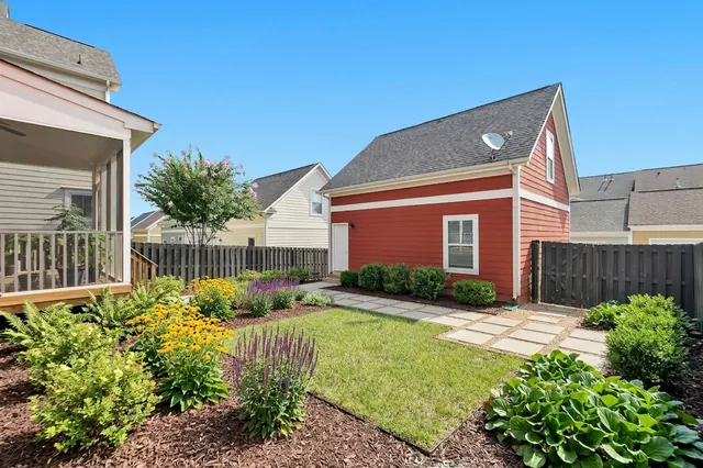 AI generated low maintenance redesign of the same view: a plain lawn with a dark timber fence, a screened porch on the left and a small red outbuilding, replanted.