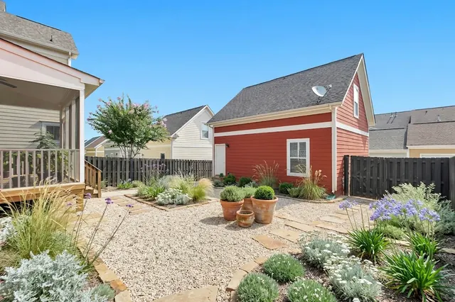 AI generated mediterranean redesign of the same view: a plain lawn with a dark timber fence, a screened porch on the left and a small red outbuilding, replanted.