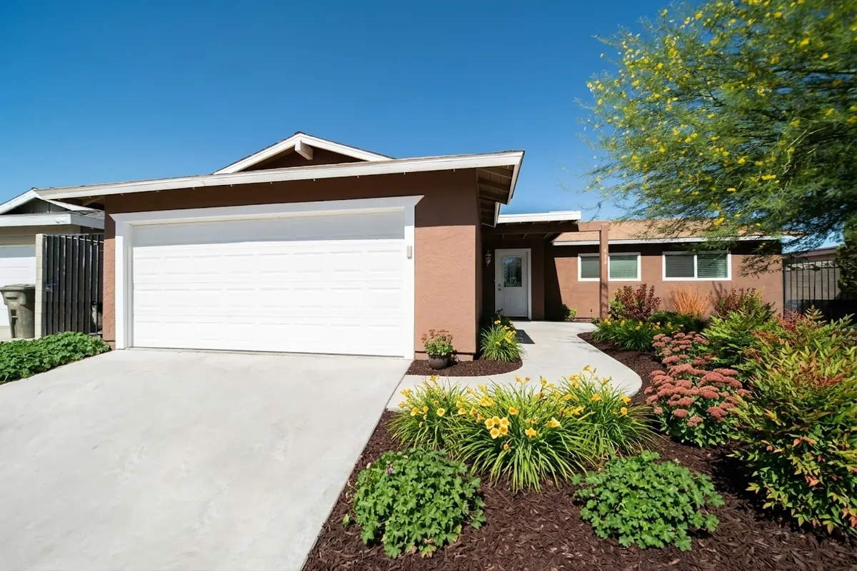 AI generated low maintenance redesign of the same view: a wide curved concrete driveway leading to a double garage on a low brick-coloured house, replanted.