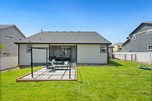Before: a back garden of mown lawn with a small concrete slab patio and metal pergola behind a single-storey house.