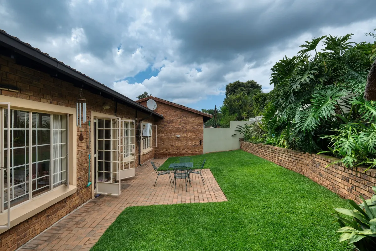 Before: a narrow side garden of lawn and a brick paved patio running along a low brick wall beside a brick house.