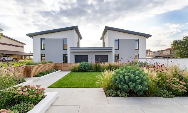 AI generated modern redesign of the same view: the rear of a new-build pair of houses with garages, a bare sandy plot and patchy new grass in front, replanted.