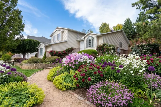 AI generated cottage redesign of the same view: a sloping lawn in front of a split-level house with a low stone retaining wall and shrub beds, replanted.